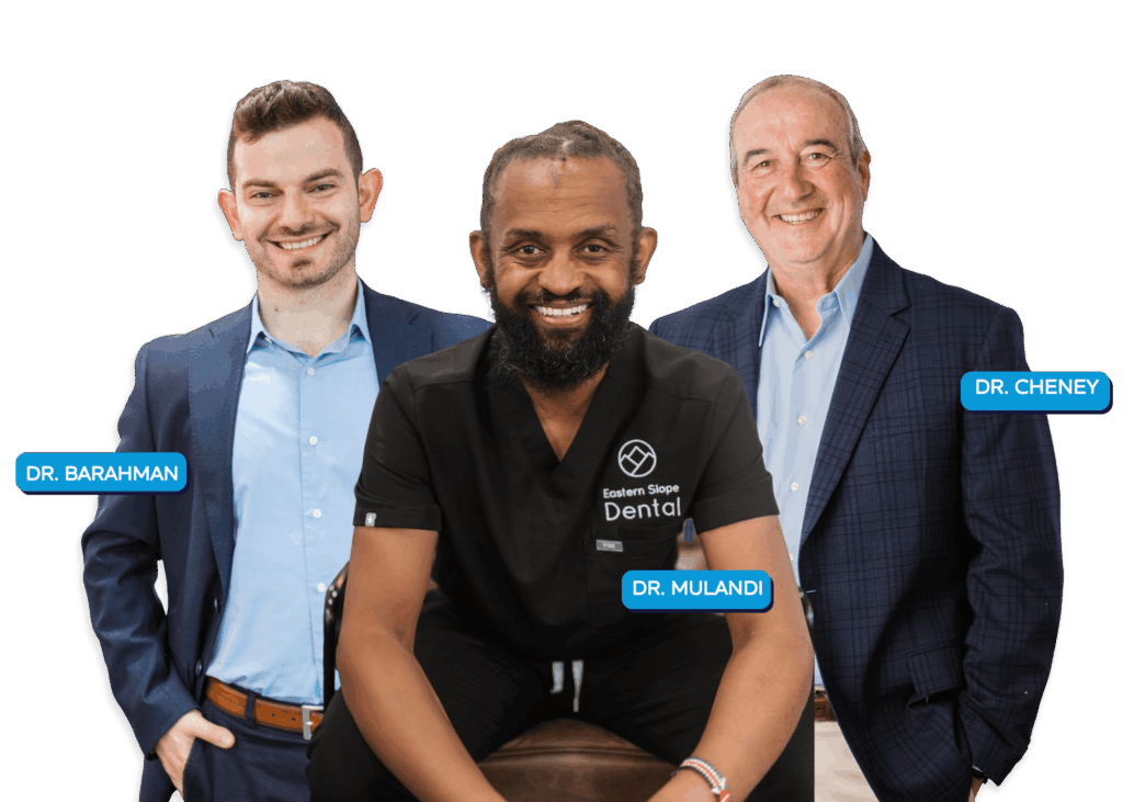 Three dental professionals pose together. Dr. Mulandi is seated in a black shirt, while Dr. Barahman and Dr. Cheney stand beside him.